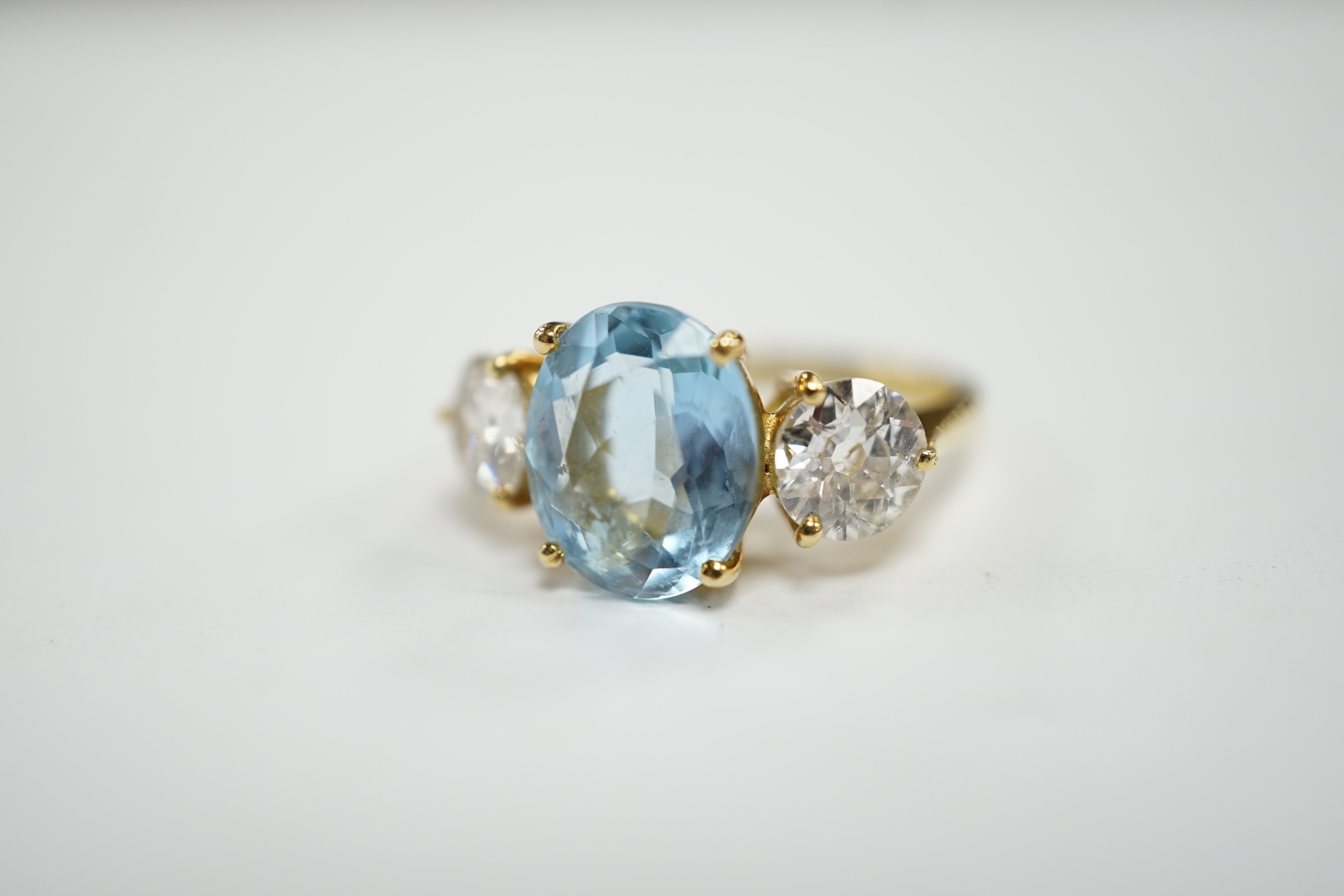 A modern 18ct gold, single stone oval cut aquamarine and two stone round brilliant cut diamond set ring, size L, gross weight 4.8 grams.